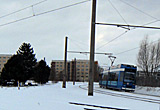 Auf diesem Bild sieht man eine Straßenbahn durch eine verschneite Landschaft fahren.