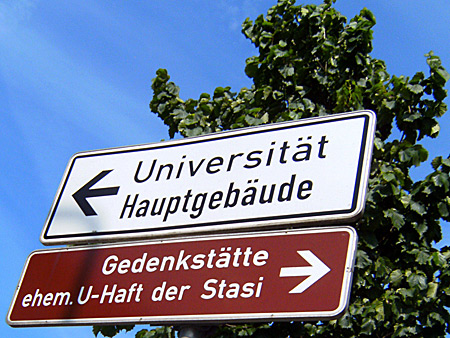 Auf diesem Bild sieht man ein Schild für die Stasi-Gedenkstätte. Darüber ein Schild zur Uni.