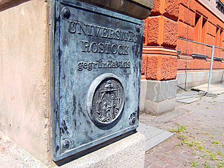Auf diesem Bild sieht man ein Bronzeschild mit dem Logo der Uni Rostock.