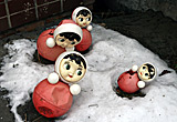Auf diesem Bild sieht man vier von diesen russischen Puppen im Schnee liegen.